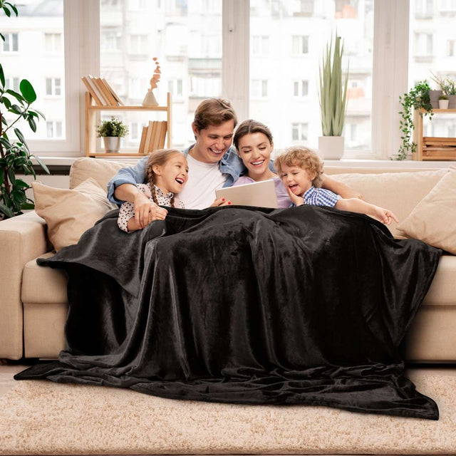 Familia reunida en un acogedor sillón, cubriéndose con una cobija matrimonial de color negro para mayor calidez y confort