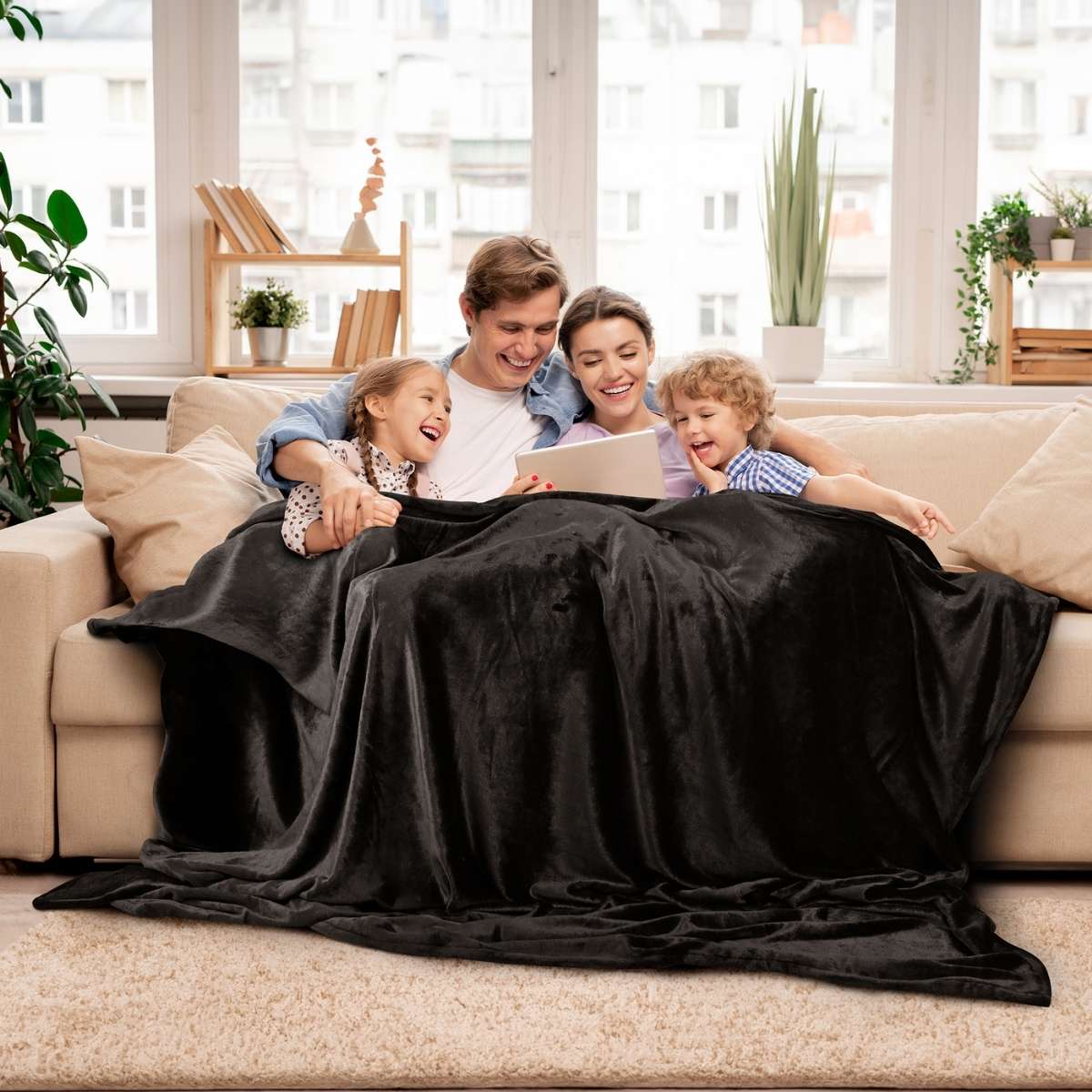Familia reunida en un acogedor sillón, cubriéndose con una cobija king size de color negro para mayor calidez y confort