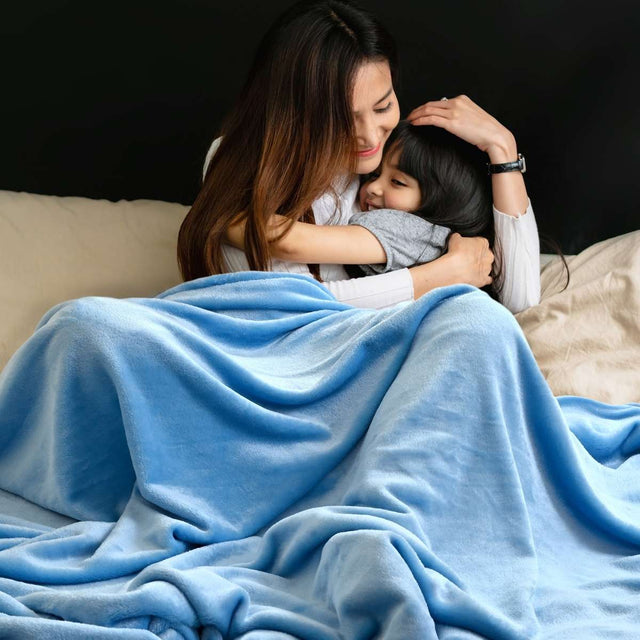 Mamá abrazando a su hijo con amor mientras están envueltos en una cobija de color turquesa, compartiendo un momento de ternura y calidez