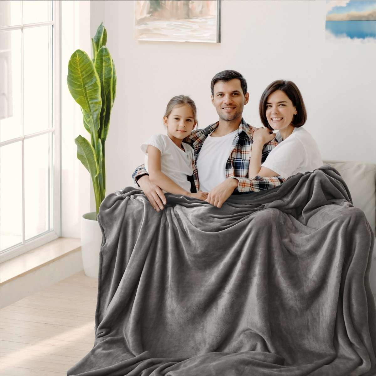 Familia reunida en un acogedor sillón, cubriéndose con una cobija de color gris claro para mayor calidez y confort