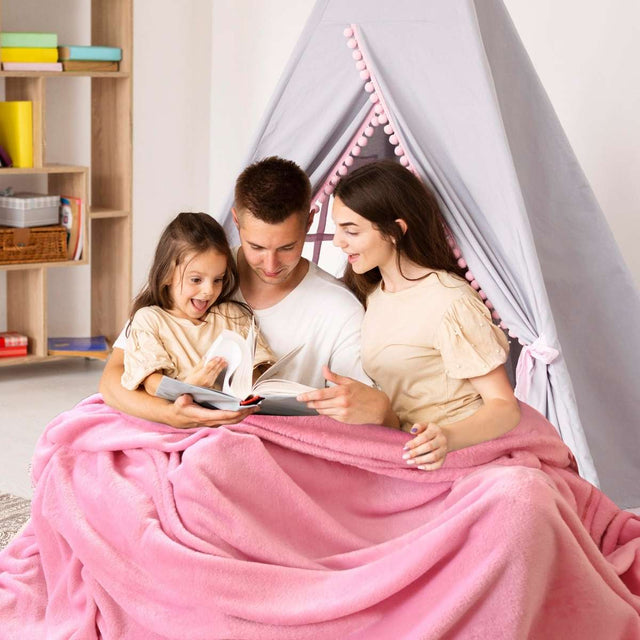 Padres sentados con su hija, compartiendo un momento de lectura bajo una acogedora cobija rosa matrimonial , disfrutando juntos de un cuento
