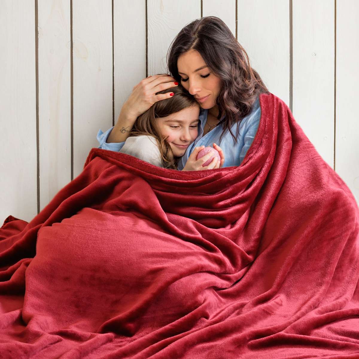 Mamá e hija compartiendo un tierno abrazo en la cama, envueltas en una cálida cobija matrimonial color vino